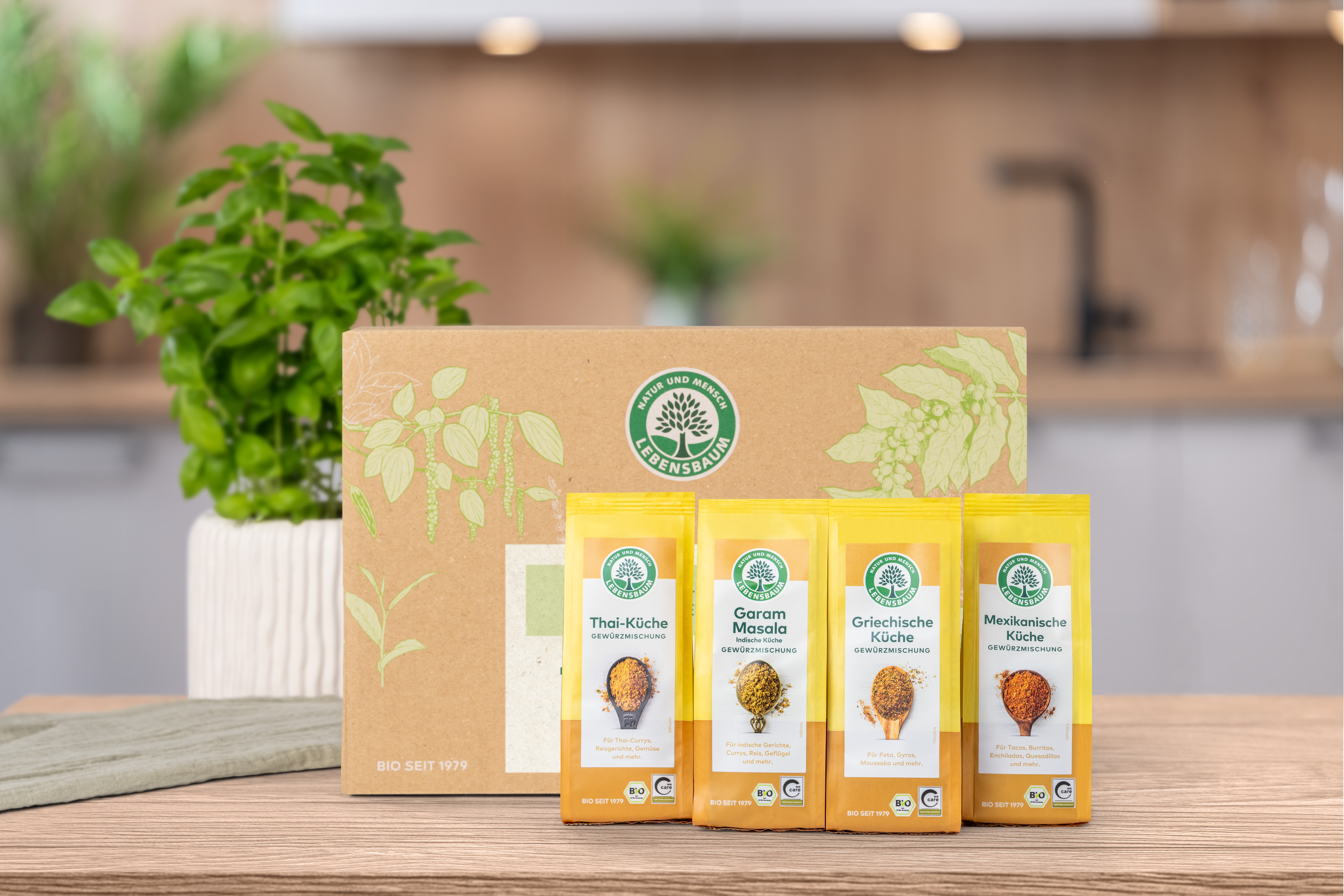 erschlossenes Geschenk-Set steht auf einem Holztisch in der Küche. Vor der Geschenk-Set Verpackung  stehen die darin enthaltenen Produkte