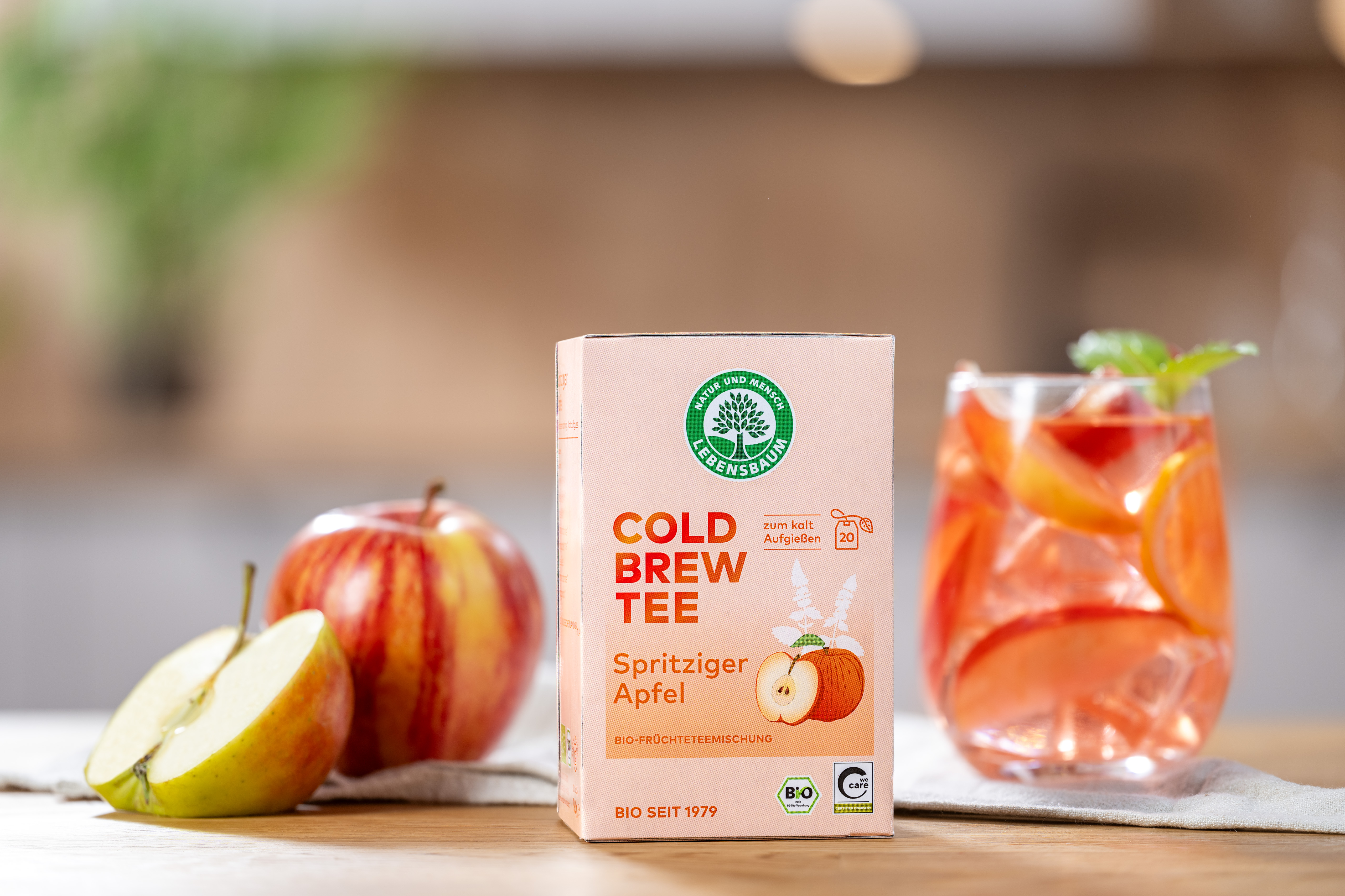 Bio-Cold-Brew-Tee Spritziger Apfel auf einem Tisch neben einem lecker aussehenden Glas n mit Cold-Brew und Eis, im Hintergrund eine Küche