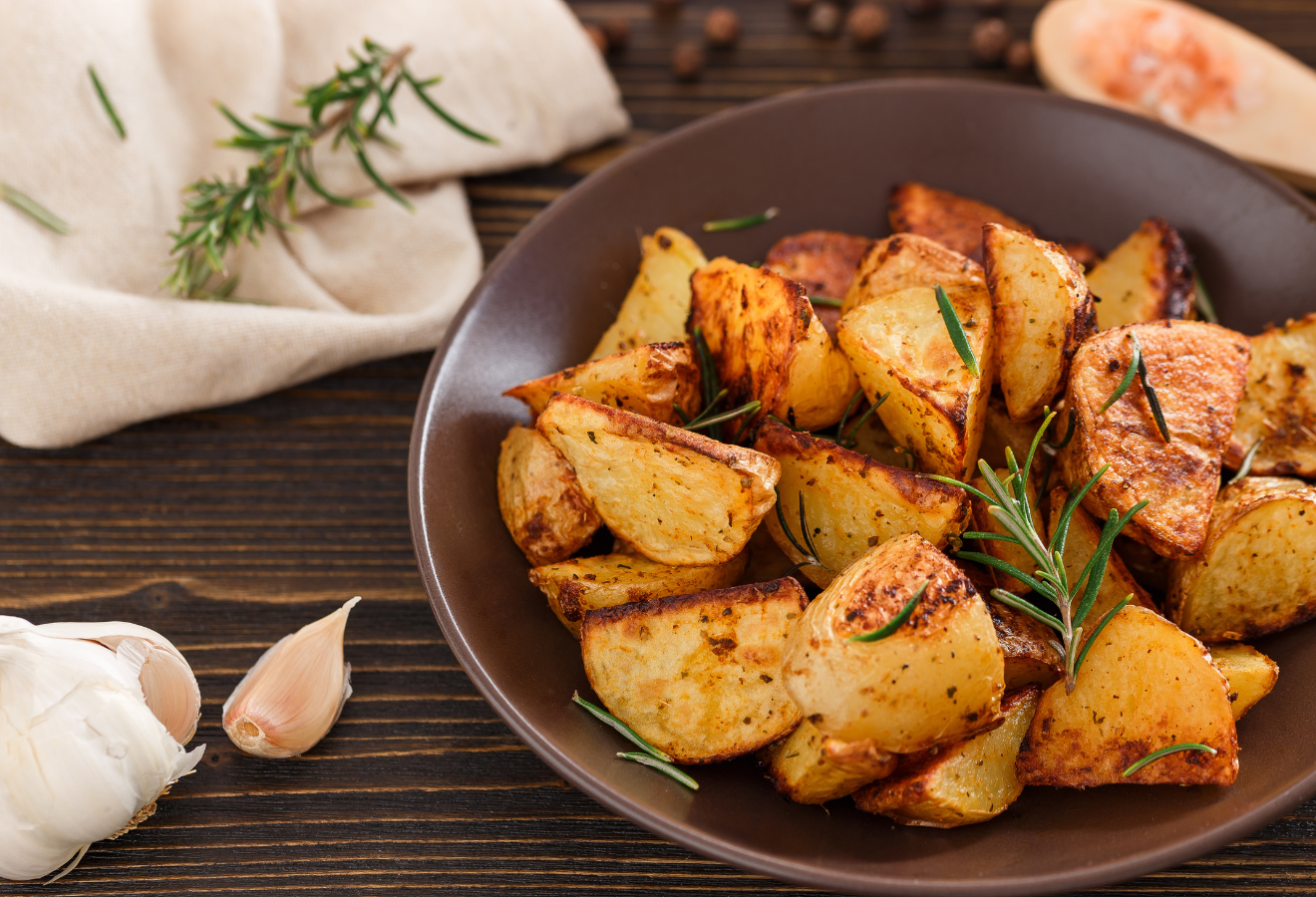 Ferdis Ofenkartoffeln in einer schwarzen Schüssel, mit Rosmarin garniert, daneben Knoblauch